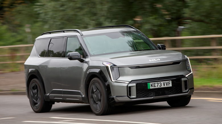 A gray 2024 Kia EV9 electric car in the GT Line trim spec driving down a British road on an overcast day.