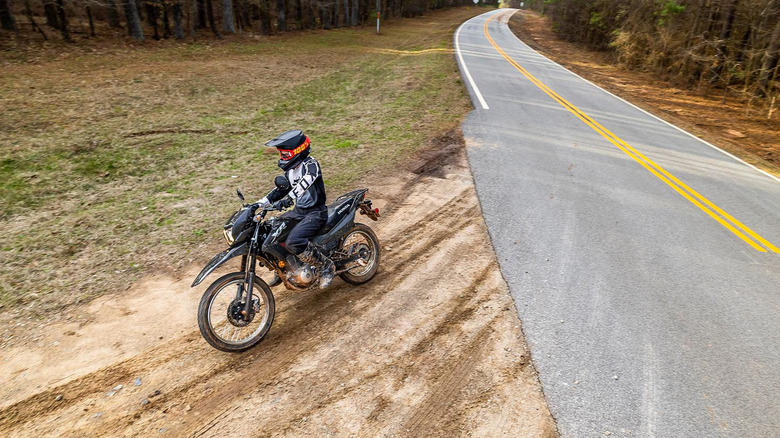 An aerial shot of a rider in black-and-white gear turning off a bitumen road onto a dirt track on a Honda XR150L.