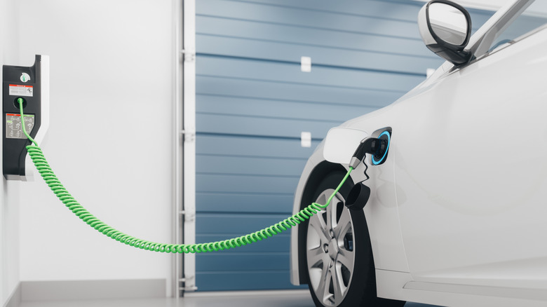 A white electric vehicle parked inside a garage and hooked up to a home wall charger