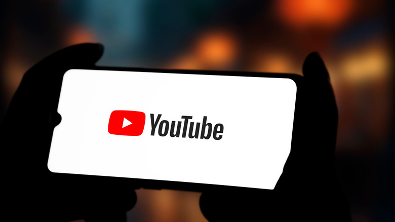 Hands holding smart phone with YouTube logo on white screen