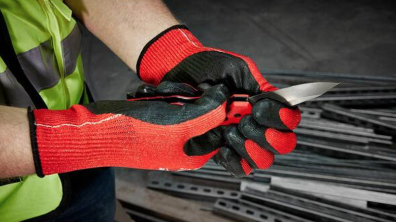 Man holding Milwaukee Fastback press and flip utility knife in gloved hands