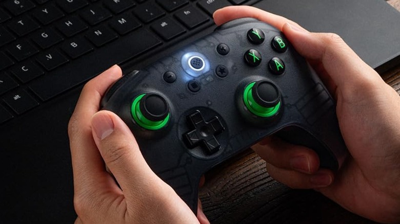 An 8BitDo Ultimate 2C gaming controller being held by a person in front of a laptop