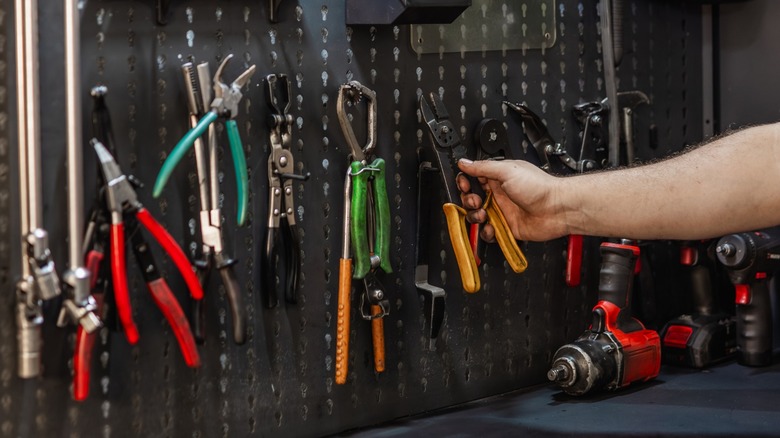 a person reaching for wire strippers on a tool peg board