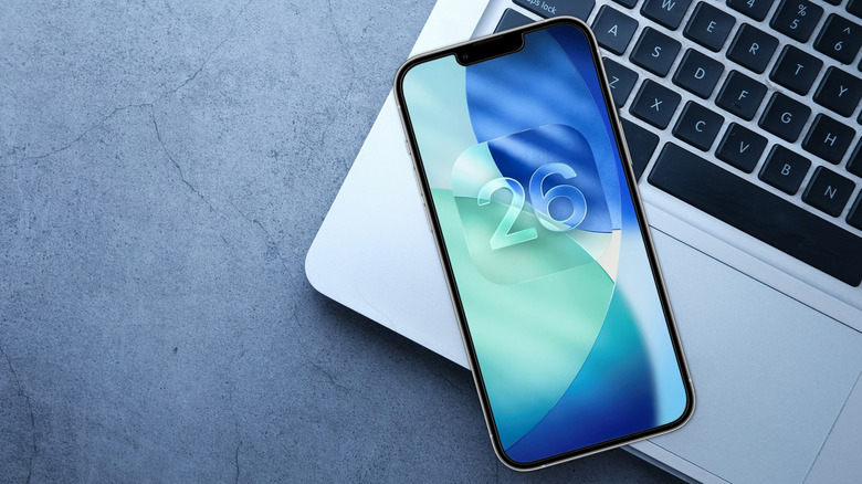iPhone screen with iOS 26 logo sitting on a laptop