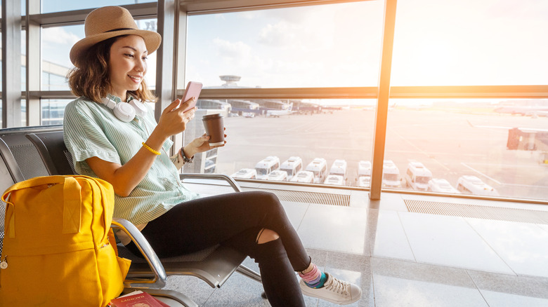 A woman waiting for her airplane in airport with passport, baggage, and smartphone.