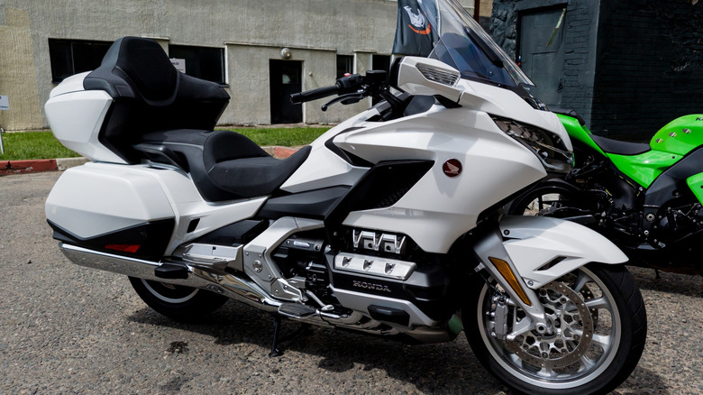 A white and gray Honda Gold Wing motorcycle parked on its kickstand at the side of a shaded street.
