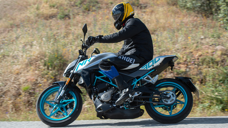 a rider in all-black gear riding a black and green CFmoto bike down a twisting road, left view visible.