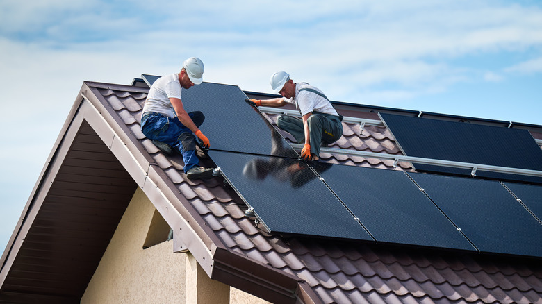2 male workers in white hard hats installing solar panels on the roof of a home