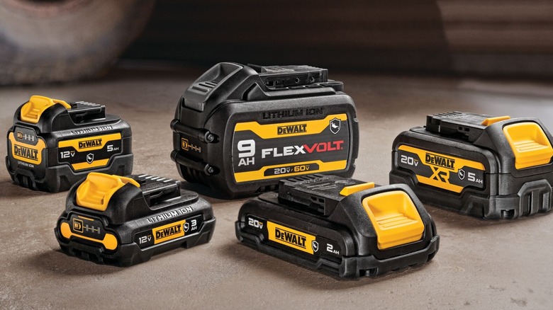 Several DeWalt batteries on a concrete floor, next to a vehicle wheel.