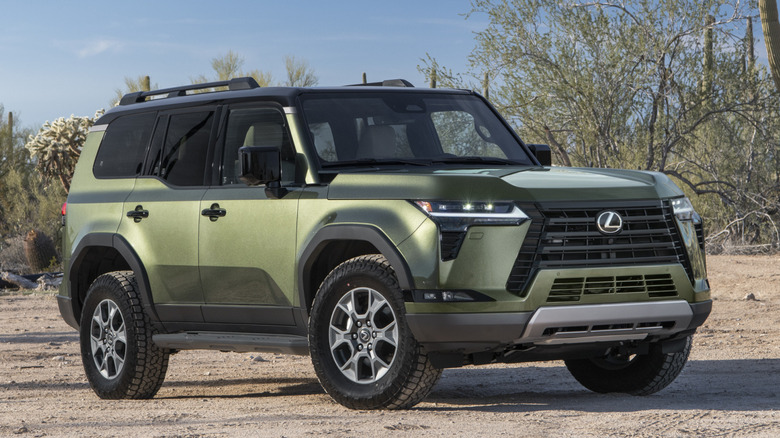 Green Lexus GX 550 parked in dirt with trees in background
