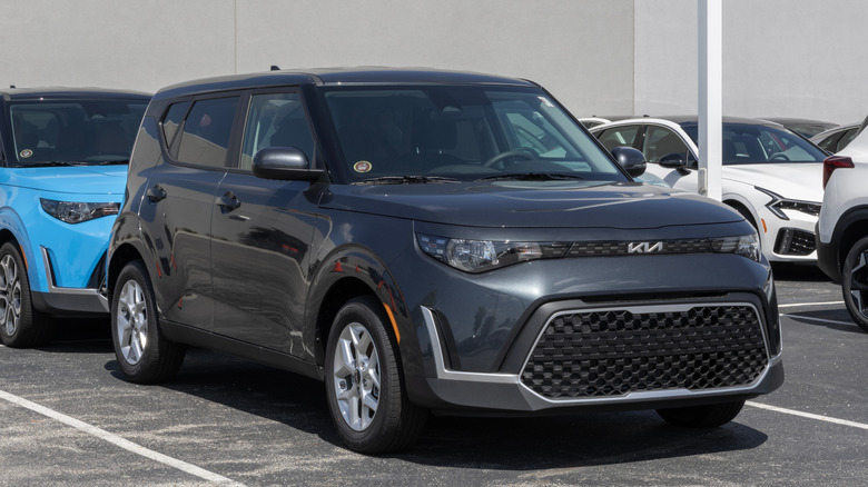 A black Kia Soul parked right outside the storefront of a Kia dealer, being an example from the new generation of cars.