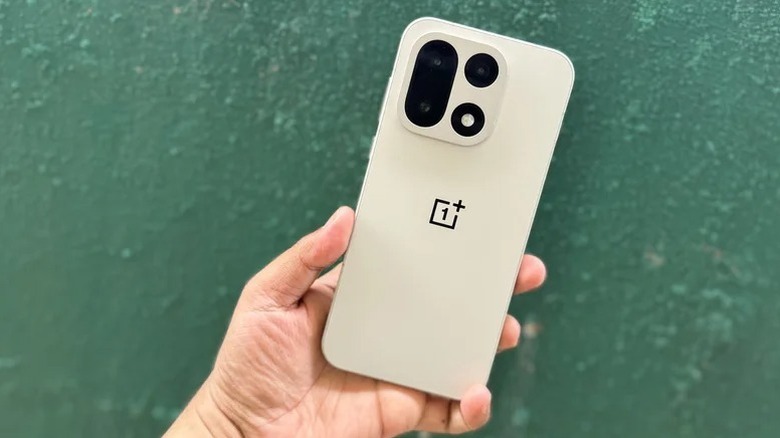 Hand holding OnePlus 15 with green wall in background